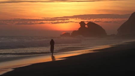 Man walking in the sunset, along the beach facing the pacific oceanの写真素材