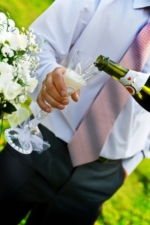 Man with necktie pouring champange to wineglass. Wedding bouquet in the left.の写真素材