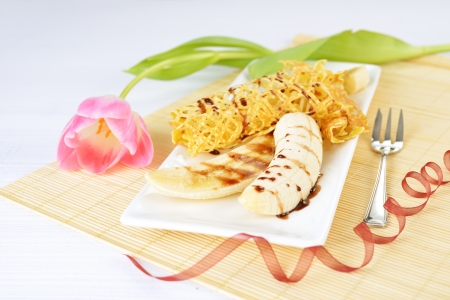 closeup image of a delicious pancakes with banana and chocolate syrup on it. Beautiful tulip flower on the background.の写真素材
