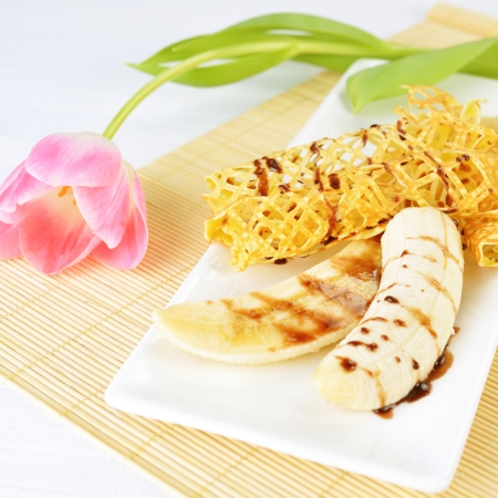 closeup image of a delicious pancakes with banana and chocolate syrup on it. Beautiful tulip flower on the background.の写真素材