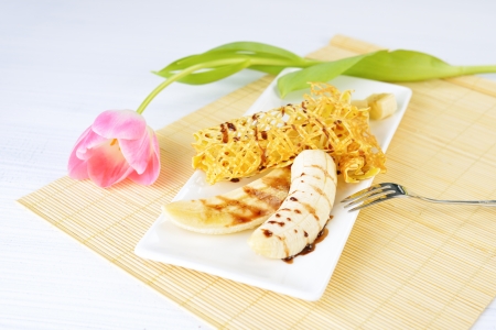 closeup image of a delicious pancakes with banana and chocolate syrup on it. Beautiful tulip flower on the background.の写真素材