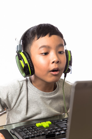 Asian kid play computer internet games and wear headset to communicateの写真素材