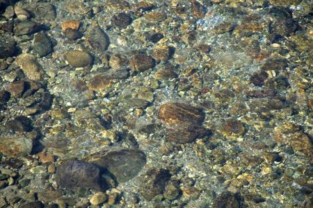 Rocks and pebbles seen through the transparent layer of crystal clear water
