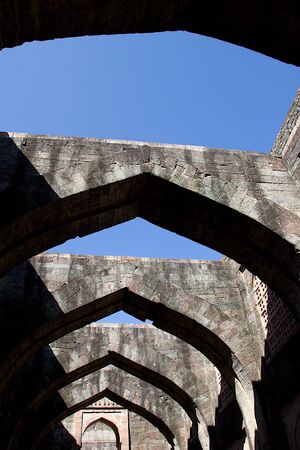 Low angle view of stone arches of Hindola Mahal or Swinging Palace audience hall with sloping side walls against blue sky, Mandu, Madhya Pradesh, India, Asiaの写真素材