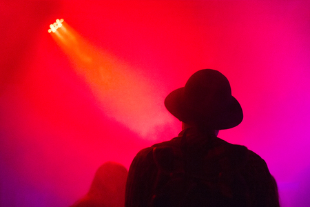Silhouette man in a hat enjoying the concert in a violet light and fogの写真素材