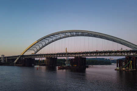Construction of a new arch bridge across the Dnipro (Dnieper) River, Kyiv, Ukraine. Sunset view of the large infrastructure facility on the waterの写真素材