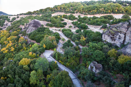 The cobblestone road, paved with stone, winds between the greenery and the stones of Meteora