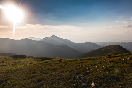 Beautiful sunrise over the mountain landscape among grassy mountain hills and meadow covered green...