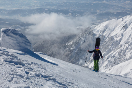 An active female freerider with a snowboard going to the top of the mount in a backcountry alpine mountain terrainの写真素材