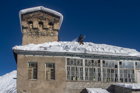 Svaneti, Georgia - 1 Feb, 2020: A man throws snow from the roof next to the Svan tower. Rural environment in Mestia, Georgiaのeditorial素材