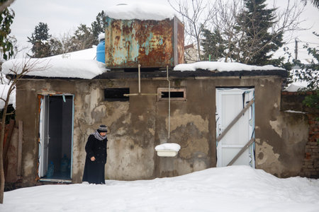 Kutaisi, Georgia - 3 Feb, 2020: An old woman against the background of the ruins of a snowy houseのeditorial素材