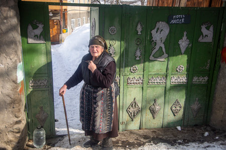 Mestia, Georgia - 1 Feb, 2020: An old woman near a gate painted in the traditional colors of Svanetiのeditorial素材