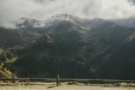 A solitary figure admires the vast, mountainous landscape amidst atmospheric clouds.