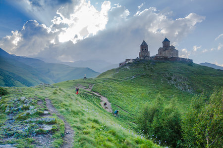 The Gergeti Trinity Church stands tall against a dramatic sky, overlooking a lush green valley....