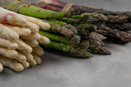 Three bunches of different fresh asparagus isolated on grey. Purple white and green asparagus. Close up.の写真素材