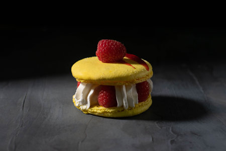 Yellow macaroon stuffed with fresh raspberries and whipped cream. French dessert.