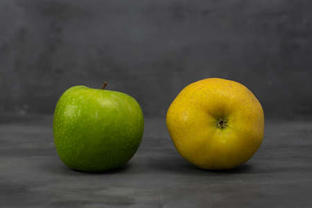 Two 2 different color apples, green and yellow on grey concrete background. Healthy life concept. Fruits.の写真素材