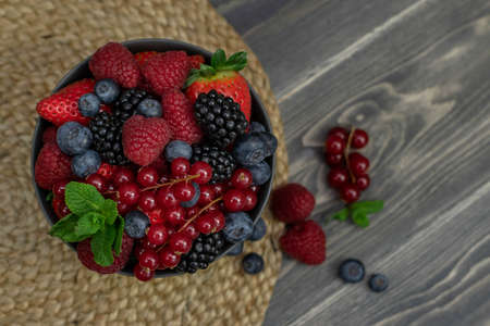 Ripe sweet different berries in bowl on wooden table. Harvest Concept. Fresh berries.