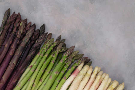Three bunches of different fresh asparagus isolated on grey. Purple white and green asparagus. Fresh vegetables.の写真素材