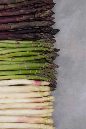Three bunches of different fresh asparagus isolated on grey. Purple white and green asparagus. Fresh vegetables.の写真素材