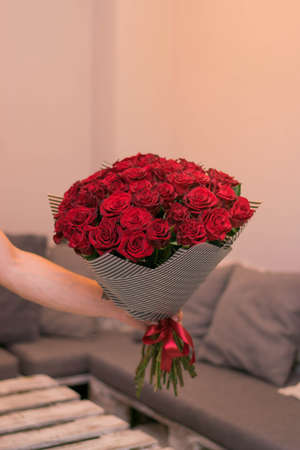 Hand holding bouquet of red roses over grey backgroundの写真素材