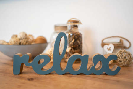 The inscription relax from on a wooden table against the background of bottles with essential oil and spicy herbs. Wellness concept and self-care background.の写真素材