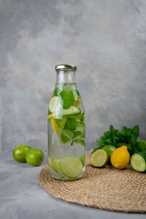 Detox Sassy water with lemon, cucumber, mint. A bottle of clean, cool and fresh drink stands on a gray concrete background with ingredients on board. Strengthening immunity, diet. Still life close up.の写真素材