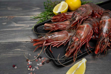 Raw black tiger shrimps on black plate and wood table, decorated with lemon slices. Fresh seafood.の写真素材