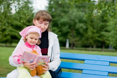 Mother and daughter reading a book on a park benchの写真素材