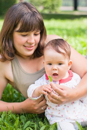happy mom with a little girl resting on the grass in the parkの写真素材