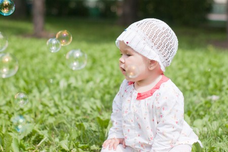 A little girl sitting on green grass in the park looking at soap bubblesの写真素材