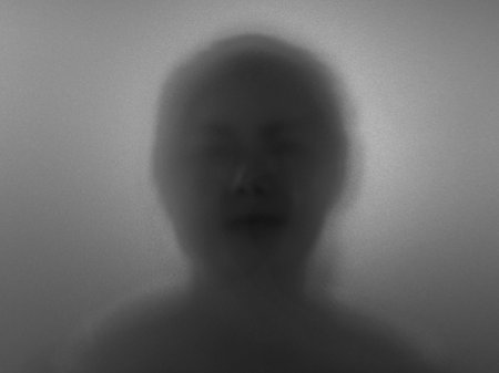 Blurry dark silhouette of a woman head behind a smoked glass partition.の写真素材