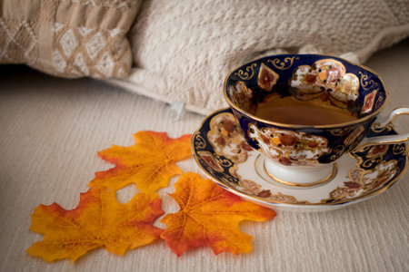Cup of tea with autumn leaves in cozy environment with ivory and white cushionsの写真素材
