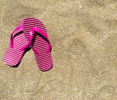 Pair of colorful sandals, slippers, on sandy beach with text spaceの写真素材