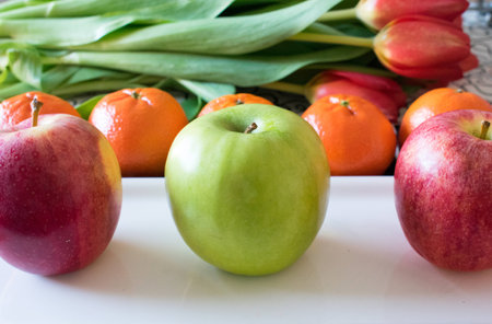 Fresh apples and clementines in white plate with tulips backgroundの写真素材