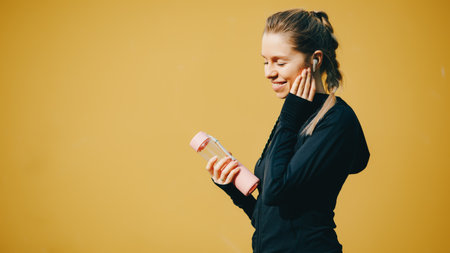 Attractive caucasian girl on yellow isolated background with wireless headphones in sport suit make...