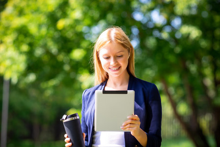 Young girl with wireless headphones in the park using tablet and smiling