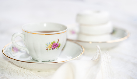 Luxury porcelain tea set with a cup, teapot, sugar bowl on white tablecloth with white bagels on a plateの写真素材