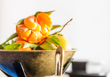 A close-up of a fresh juicy clementines with green leaves in a scale bowlの写真素材