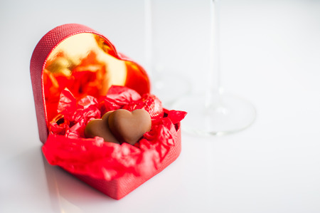 Chocolate hearts in red heart-shaped box ,  and two glasses of pink champagne. white background. selective focus.の写真素材