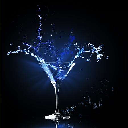 Colorful cocktail splashes falling into a martiny glass on dark background party club entertainment. Copy space.の写真素材