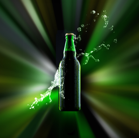 A bottle of beer with condensed water drops on its surface and a splash of liquid lit by radial colorful light raysの写真素材