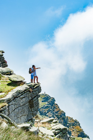 Travel concept: young tourists couple with backpacks standing on the top of a cliff with approaching puffy white cloud. Copy space.の写真素材