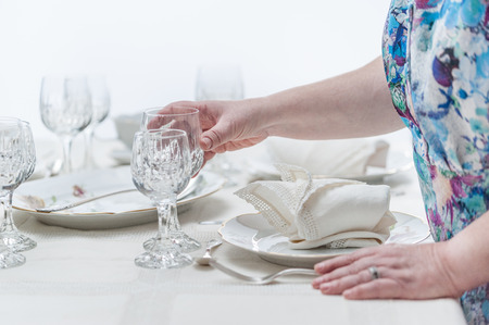 Women hands serving a crystal glassware of a table served with porcelain dinnerware. and vintage...