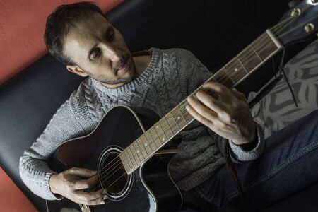 Man playing acoustic guitar in his room lying on the bedの写真素材