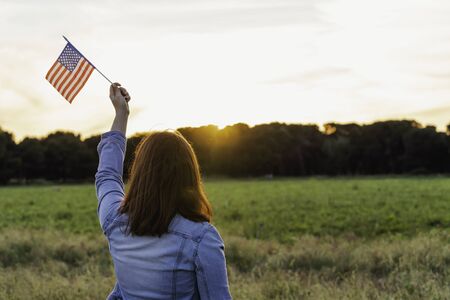 Young happy woman from behind with the United States flag enjoying sunset in nature. 4th of july independence day of the united statesの写真素材