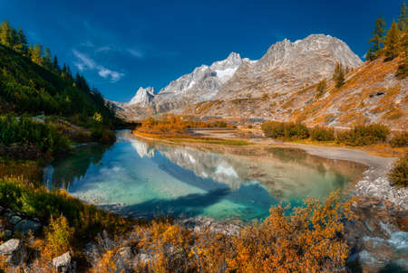 colors of autumn season into the wild Val Veny with lake in foreground, Aosta Valley, Italyの写真素材