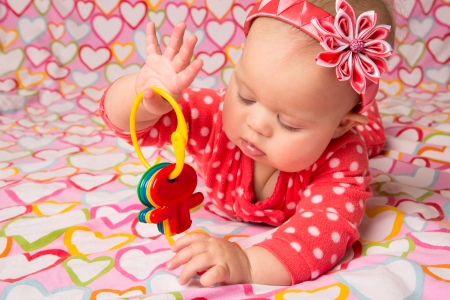 An adorable baby girl wearing a red headband with a decorative flower, playing with toy keysの写真素材