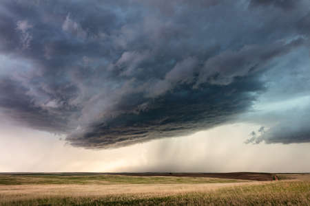Storm clouds with rain falling over rolling grasslands in Montanaの写真素材