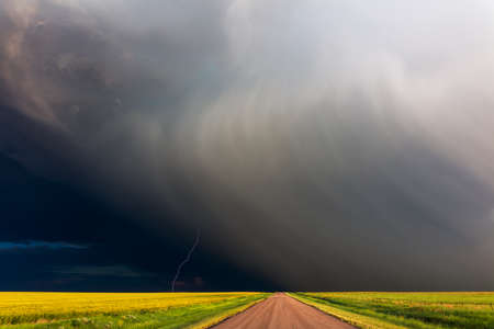 Weather background with thunderstorm, lightning and dramatic storm clouds over a dirt road and farm...
